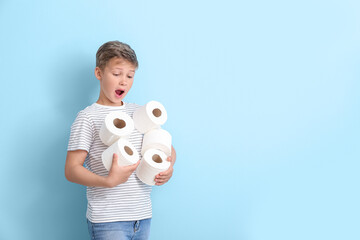 Fototapeta na wymiar Shocked little boy with many rolls of toilet paper on blue background