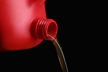 Pouring of motor oil from canister against black background, closeup