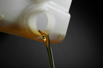 Pouring of motor oil from canister against black background, closeup