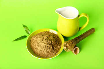 Saucer with hojicha powder, jug of milk and chasen on green background
