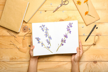 Female hands with dried pressed flowers in book on wooden background