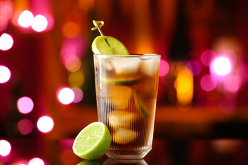 Glass of tasty Cuba Libre cocktail on table against blurred lights