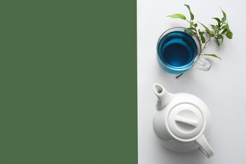 Teapot and glass cup of organic blue tea on color background
