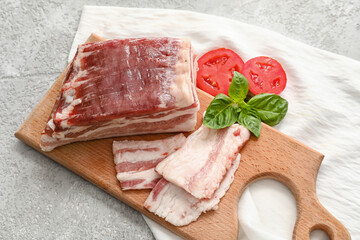 Wooden board with uncooked bacon on light background