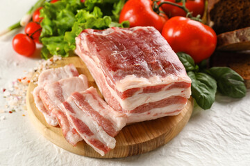 Wooden board with uncooked bacon on white background
