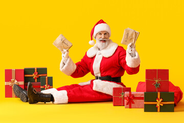 Santa Claus with letters and gifts on yellow background