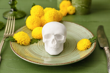 Fototapeta na wymiar Table setting with human skull for Mexico's Day of the Dead (El Dia de Muertos) and flowers on green wooden table