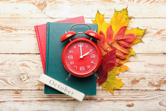 Alarm clock, notebooks and autumn leaves on wooden background