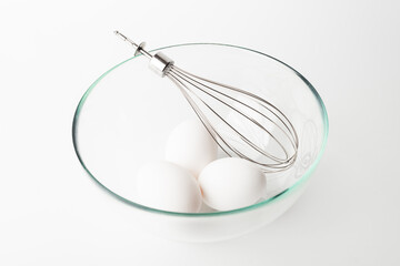 whisk and chicken eggs on white background 
