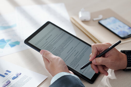 Hands of businessman reading agreement on tablet computer and signing with digital pen