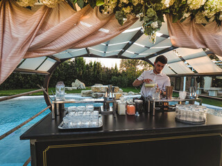 young caucasian bartender at work in a cocktail station outdoors in a location venue in a party at...
