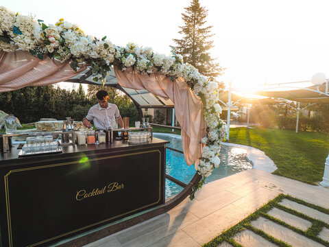 young caucasian bartender at work in a cocktail station outdoors in a location venue in a party at sunset