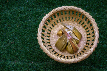 Thai dessert steamed flour with coconut filling stuffed in banana leaf (Kanom Sai Sai) and coconut leaf on basket, Thai Traditional Dessert, Top view, copy space.