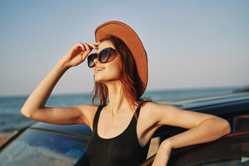 cheerful woman in sunglasses and a hat on the ocean near the car