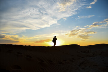 A man walks on the sand against the sky.
