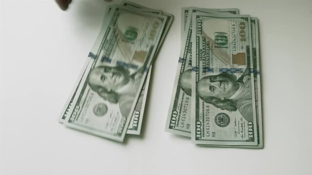 Splitting money into two equal stacks. Men's hand puts hundred-dollar bills on the table, and then takes them away. Fast motion.