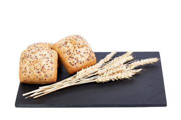 Bread rolls with seeds next to some ears of wheat on a black slate board