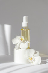 Obraz na płótnie Canvas Mock-up of glass bottle with essential oil, standing on white jar with cream, surrounded by orchid flowers. Vertical white background with morning sun rays. Concept of beauty industry, spa treatments