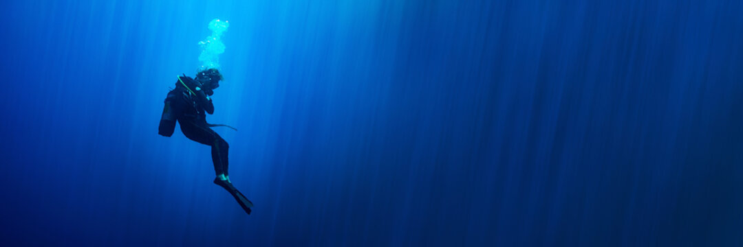 Background banner with a scuba diver woman standing still in deep blue with sun rays
