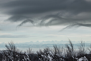 Wide panoramic view of the Swiss Alps from the Vosges mountain range in France during winter covered with snow with curly clouds