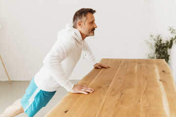 Middle-aged man exercising push-ups on a table at home