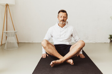 Senior man sitting on yoga mat meditating with serene expression