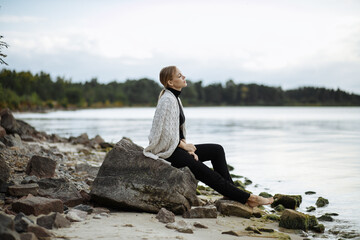 a girl in black with a light cape on her shoulders walks barefoot along the seashore