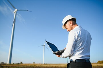 Engineer standing and hoding laptop with wind turbine.