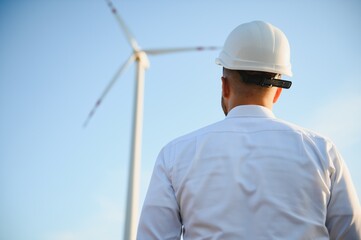 Engineer is checking energy production on wind turbine. Worker in windmills park in helmet.
