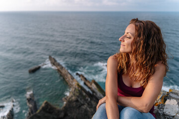 Fototapeta na wymiar Panoramic top view of woman with eyes closed on holidays in Asturias. Horizontal view of cheerful woman isolated in blue sea in the background. Travel on holidays and people concept.