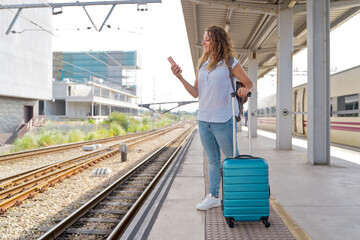 Horizontal view of woman walking in train platform with smartphone. Caucasian woman using technology and traveling in public transport. Travel and technology concept.