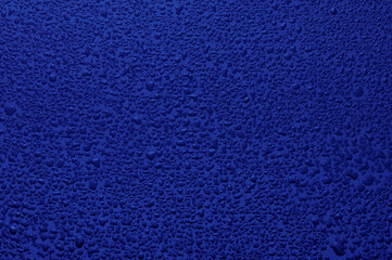 Water drops on black glass. Background illuminated with dark blue ​light.