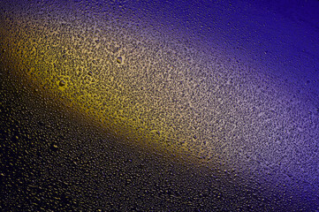 Water drops on black glass. Background illuminated with dark blue and yellow ​light.