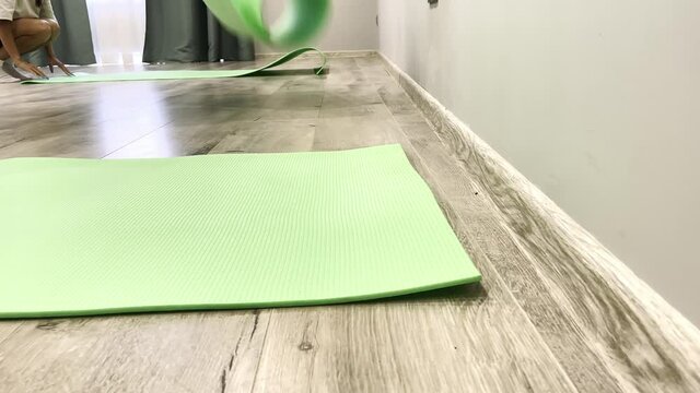 Young women put colorful green mats onto wooden floor preparing for yoga training in spacious gym close view