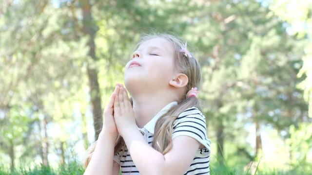 Cute happy little girl closed her eyes and prays outdoors