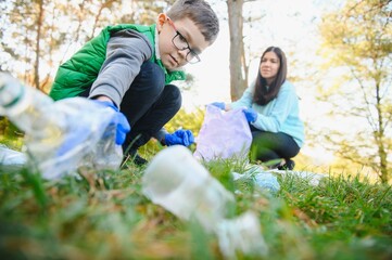 Smiling boy picking up trash in the park with his mother. Volunteer concept.