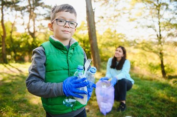 Smiling boy picking up trash in the park with his mother. Volunteer concept.