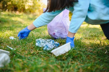 women's hands in red rubber gloves. Woman collects trash in the bag. Volunteer scavenge garbage in the summer park. Nice progressive woman making an effort to help the environment