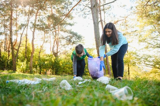 Mom teaches her son to clean up trash in nature. A woman removes plastic bottles in a bag. The topic of environmental pollution by garbage.