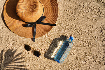 Fototapeta na wymiar Ocean or sea shore, wicker hat lying on the sand, palm leaf shadow next to bottle of fresh water