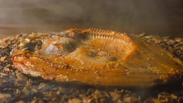 Cooking smoked ide fish with seasonings and crispy crust on decayed shavings and charcoals with floating steam in smokehouse macro slow motion