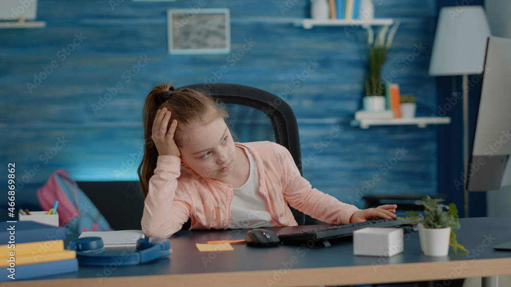 Poster exhausted child looking at computer for online classes while sitting at desk. little girl feeling ti