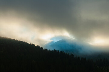 Naklejka na ściany i meble The rays of the rising sun break through the morning fog in the mountains. Silhouette landscape photo