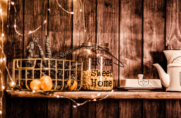 A glass jar with cornflakes and tangerines in a vase stands on a wooden shelf decorated with Christmas decor