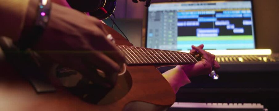 Tilt up close up shot of African American musician with dreadlocks sitting in recording studio and playing guitar
