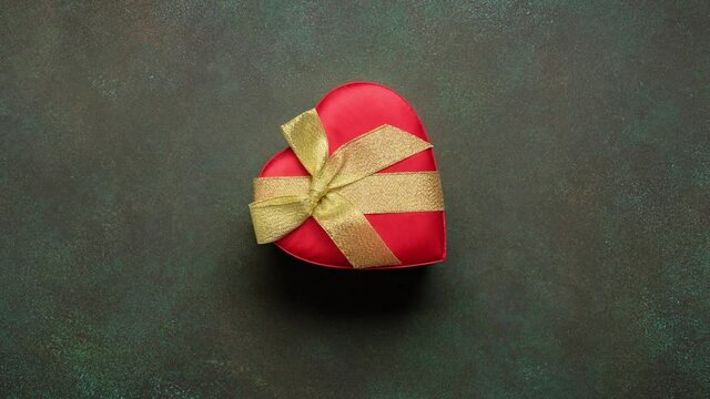 Christmas red heart-shaped gift box with golden bow appears in the frame and disappears. Green background. Stop mption animation.