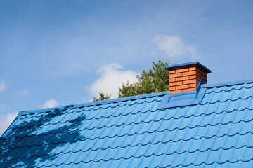 A blue tin roof along with a brick chimney against a blue sky with clouds.
