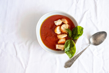 Top view of Spanish tomato soup, gazpacho  served in the bowl with bread crumbs and decorated with fresh basil.