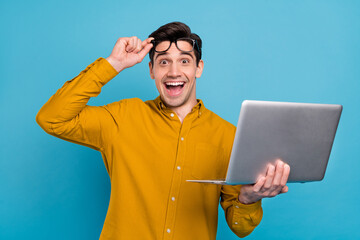 Photo of excited amazed funky geek guy hold pc take off specs wear yellow shirt isolated blue color...