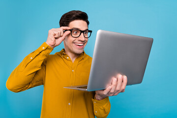 Photo of funny geek nerd guy hold pc look screen wear eyewear yellow shirt isolated blue color...